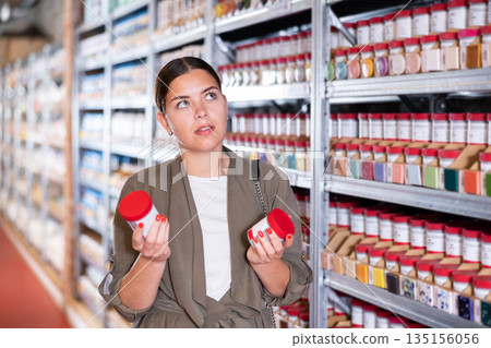 Female shopper choosing pottery glaze jars in pottery specialty store 135156056
