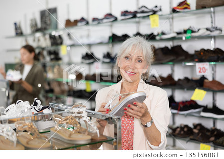 Elderly woman chooses sandals in shoe store Elderly woman chooses sandals in shoe store 135156081