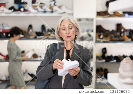 Senior woman takes samples from showcase and examines snickers Senior woman takes samples from showcase and examines snickers 135156083
