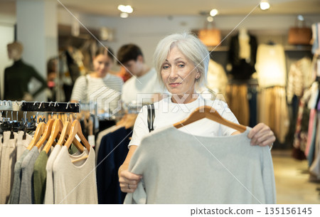 Old woman choosing convenient jumper in clothing store 135156145