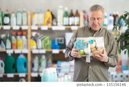 Senior man studies label and choose shower cosmetic present, packaged in basket. 135156146