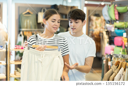 Girl and young male friend talk over about fashion of cotton trousers while shopping at mall Girl and young male friend talk over about fashion of cotton trousers while shopping at mall 135156172