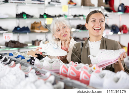 Young colleague shows elderly lady advantages of thick sole in modern sneakers Young colleague shows elderly lady advantages of thick sole in modern sneakers 135156179