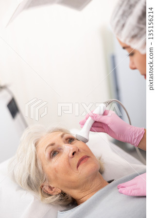 Old woman having face laser therapy procedure Old woman having face laser therapy procedure 135156214