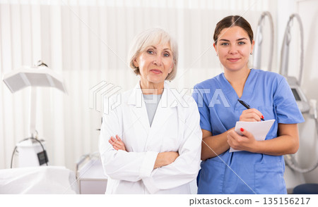 Smiling woman doctors posing against background of cosmetology devices Smiling woman doctors posing against background of cosmetology devices 135156217