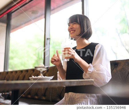 Smiling young woman with a drink in hand by the window in a cafe 135156946