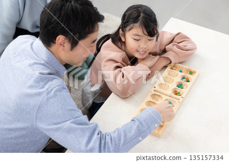 An elementary school girl playing Mancala with her father in the living room at home An elementary school girl playing Mancala with her father in the living room at home 135157334