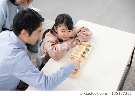 一位小學生在家裡的客廳和父親玩曼卡拉棋。 135157335