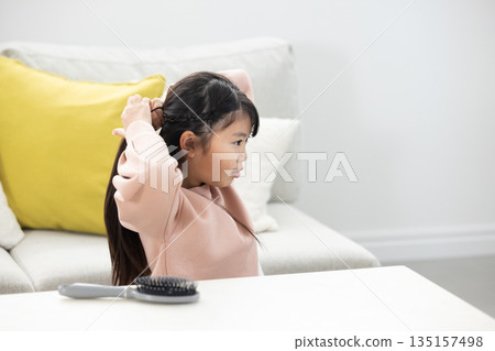 Elementary school girl tying her hair in the living room 135157498
