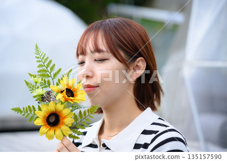 一位神態放鬆的女士正在聞向日葵的香氣。 (圖片由沖繩海濱度假村雅提供) 一位神態放鬆的女士正在聞向日葵的香氣。 (圖片由沖繩海濱度假村雅提供) 135157590