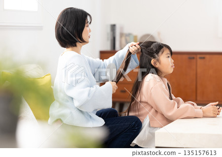 一位小學生在家裡的客廳請媽媽幫她梳頭。 135157613