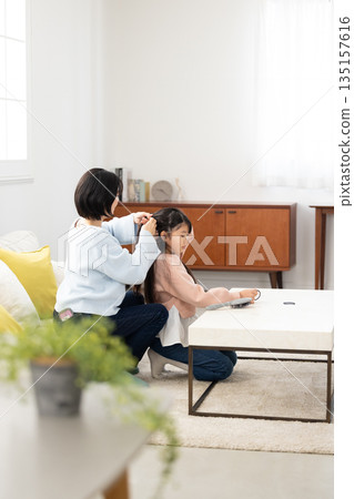 一位小學生在家裡的客廳請媽媽幫她梳頭。 135157616