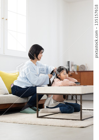 一位小學生在家裡的客廳請媽媽幫她梳頭。 135157618