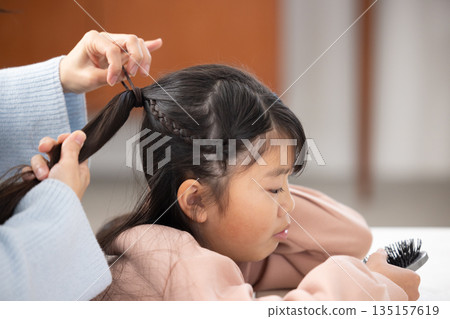 一位小學生在家裡的客廳請媽媽幫她梳頭。 135157619