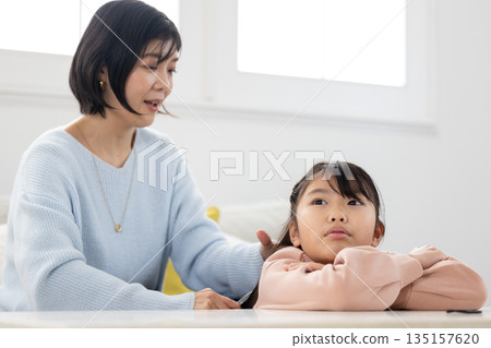 An elementary school girl having her hair styled by her mother in the living room at home An elementary school girl having her hair styled by her mother in the living room at home 135157620