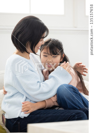 A mother and her elementary school daughter interacting on the living room sofa A mother and her elementary school daughter interacting on the living room sofa 135157658