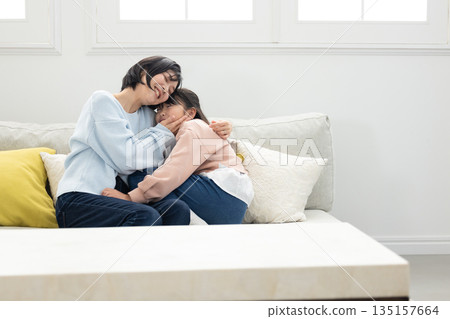 A mother and her elementary school daughter interacting on the living room sofa 135157664