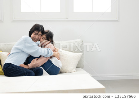 一位母親和她的小學生女兒在客廳沙發上互動 一位母親和她的小學生女兒在客廳沙發上互動 135157666