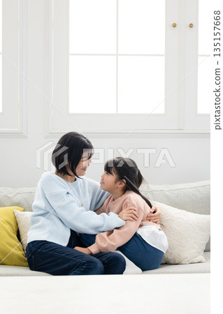 一位母親和她的小學生女兒在客廳沙發上互動 135157668