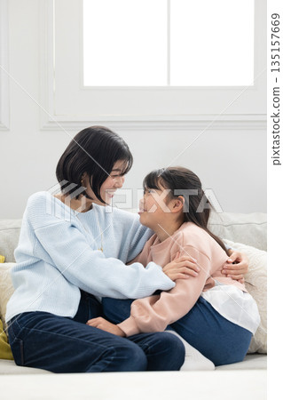 一位母親和她的小學生女兒在客廳沙發上互動 135157669