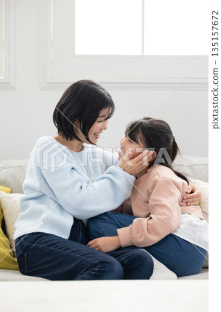 一位母親和她的小學生女兒在客廳沙發上互動 135157672