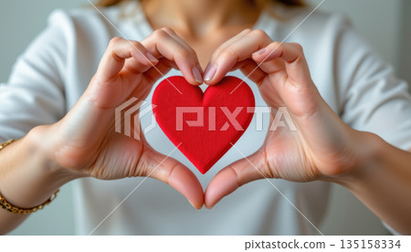 Woman making hands in heart shape holding red heart symbol of love and care with blurred background 135158334