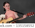 Confident female guitarist concentrating on strumming acoustic guitar and looking down at guitar neck while learning to play an instrument. Authentic musician wearing eyeglasses, dressed in pink shirt Confident female guitarist concentrating on strumming acoustic guitar and looking down at guitar neck while learning to play an instrument. Authentic musician wearing eyeglasses, dressed in pink shirt 135158552