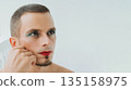 adult gay man with makeup and cosmetics on his face. A handsome transgender male with red lipstick on lips and mascara on eyes on white background 135158975