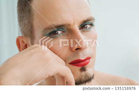 portrait of feminine gay man with makeup and cosmetics on face. A handsome transgender male with red lipstick on lips and mascara on eyes on white background portrait of feminine gay man with makeup and cosmetics on face. A handsome transgender male with red lipstick on lips and mascara on eyes on white background 135158976