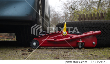 Red Hydraulic Car Jack Lifts Car During Tire Change With Spare Tire Nearby Red Hydraulic Car Jack Lifts Car During Tire Change With Spare Tire Nearby 135159349
