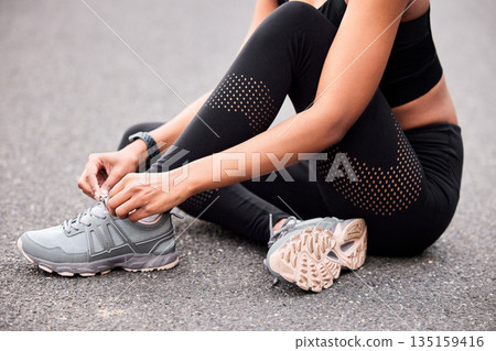 Fitness, woman tying shoes and sitting road for safety during outdoor marathon training. Running, cardio health and wellness, female athlete fixing laces on footwear and feet of runner on asphalt. Fitness, woman tying shoes and sitting road for safety during outdoor marathon training. Running, cardio health and wellness, female athlete fixing laces on footwear and feet of runner on asphalt. 135159416