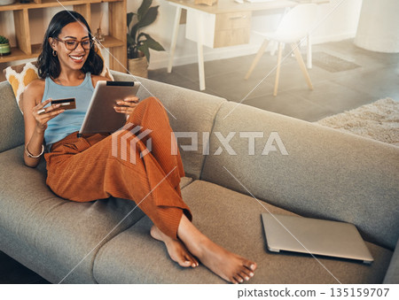 Ecommerce, credit card and woman on a sofa, tablet and transactions with online shopping, home and relax. Female person, happy client or customer on a sofa, technology or buying with internet banking 135159707
