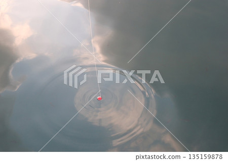 海面上倒映著雲朵、釣線和浮標。 海面上倒映著雲朵、釣線和浮標。 135159878