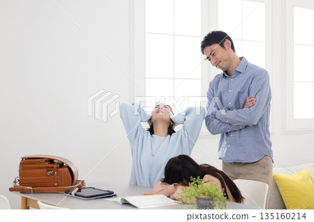 An elementary school student with his face down on the table while studying at home and his parents with troubled expressions An elementary school student with his face down on the table while studying at home and his parents with troubled expressions 135160214