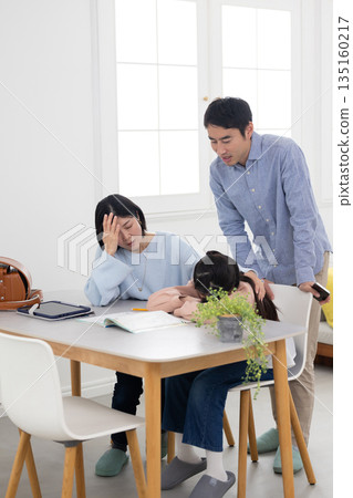 An elementary school student with his face down on the table while studying at home and his parents with troubled expressions An elementary school student with his face down on the table while studying at home and his parents with troubled expressions 135160217