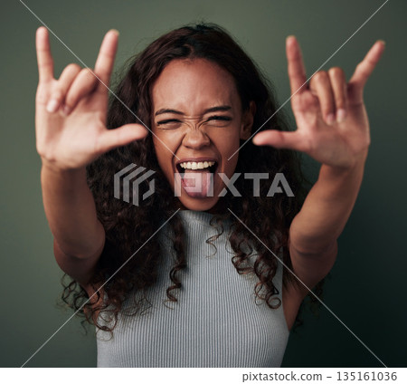 Female person, hand and rock in green studio background to celebrate with tongue in africa. Woman, rocker and sign with shouting and crazy expression for a party with excited youth for celebration. Female person, hand and rock in green studio background to celebrate with tongue in africa. Woman, rocker and sign with shouting and crazy expression for a party with excited youth for celebration. 135161036