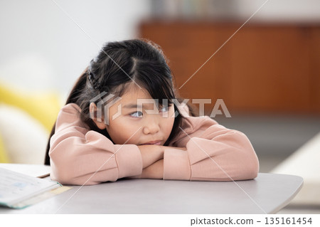 一個表情悲傷的小學生女孩躺在桌上 135161454