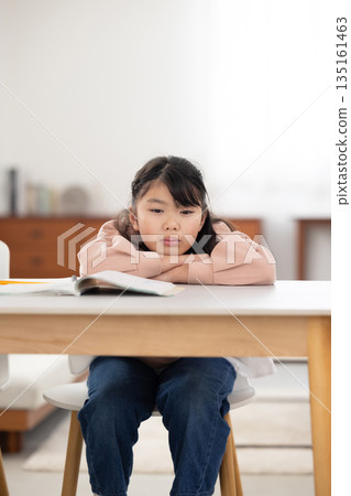 An elementary school girl with a sad expression lying on the table An elementary school girl with a sad expression lying on the table 135161463