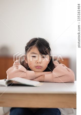 一個表情悲傷的小學生女孩躺在桌上 135161464