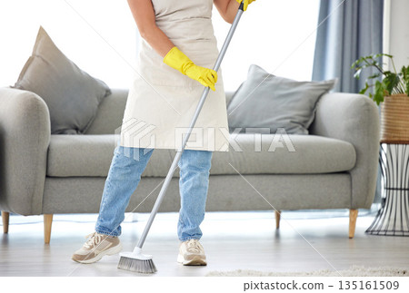 Cleaning, broom and sweeping with a housekeeper in the living room of a home for housework or chores. Floor, sweep and housekeeping with a cleaner in a house to tidy for hygiene during a spring clean 135161509