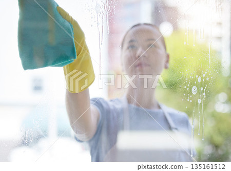 Wipe, window and cleaning with a woman housekeeper using disinfectant to remove bacteria in a home. Safety, glass and hygiene with a young female cleaner working in a domestic house for service Wipe, window and cleaning with a woman housekeeper using disinfectant to remove bacteria in a home. Safety, glass and hygiene with a young female cleaner working in a domestic house for service 135161512