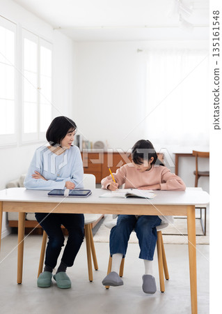 A mother watching over an elementary school girl studying at home 135161548