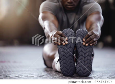 Stretching, feet and exercise with a man at gym for fitness, muscle and training workout. Athlete person with hands on shoes for warm up, goals and performance motivation on floor at a wellness club Stretching, feet and exercise with a man at gym for fitness, muscle and training workout. Athlete person with hands on shoes for warm up, goals and performance motivation on floor at a wellness club 135161592