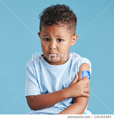 Portrait, sad and kid with arm bandage in studio isolated on a blue background. Face, upset and child with plaster after vaccine, injury or wound for healthcare wellness, first aid or medical help. Portrait, sad and kid with arm bandage in studio isolated on a blue background. Face, upset and child with plaster after vaccine, injury or wound for healthcare wellness, first aid or medical help. 135161895