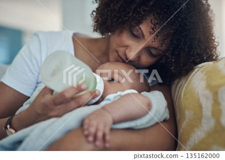 Care, woman feeding her baby with bottle and in living room on the sofa at their home. Family love, drinking or nutrition and black mother feed her newborn child on couch of their house with formula 135162000