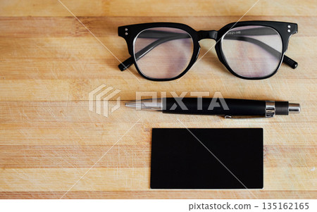 Glasses, pen and notebook on a desk in empty office for abstract background, business and vision. Eye sight, ideas and planner or journal on wooden table for reading and creative writing mockup space Glasses, pen and notebook on a desk in empty office for abstract background, business and vision. Eye sight, ideas and planner or journal on wooden table for reading and creative writing mockup space 135162165