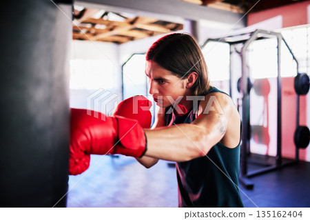 Punching bag, man and boxing in gym for exercise, workout or training for fight. Boxer, sports and serious fitness athlete punch for challenge, competition or exercising body for martial arts power. Punching bag, man and boxing in gym for exercise, workout or training for fight. Boxer, sports and serious fitness athlete punch for challenge, competition or exercising body for martial arts power. 135162404