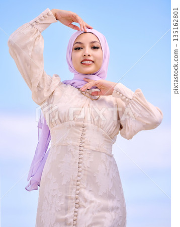 Portrait, fashion or faith with a happy muslim woman on a blue sky background in a scarf for style. Islam, religion and hijab with a trendy young saudi person posing outside in contemporary clothes 135162801