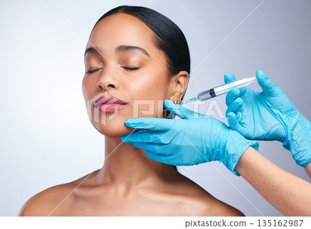 Woman, studio and gloves with needle, surgery or cosmetics for skin, facial or collagen by white background. Girl cosmetic surgeon and filler on face, syringe or hands for beauty, skincare or change Woman, studio and gloves with needle, surgery or cosmetics for skin, facial or collagen by white background. Girl cosmetic surgeon and filler on face, syringe or hands for beauty, skincare or change 135162987