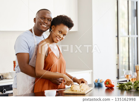 Portrait, hug and black couple in a kitchen for cooking, meal and bonding in their home together. Food, face and happy woman and man with love preparing dinner with bread, nutrition and vegetable 135162998